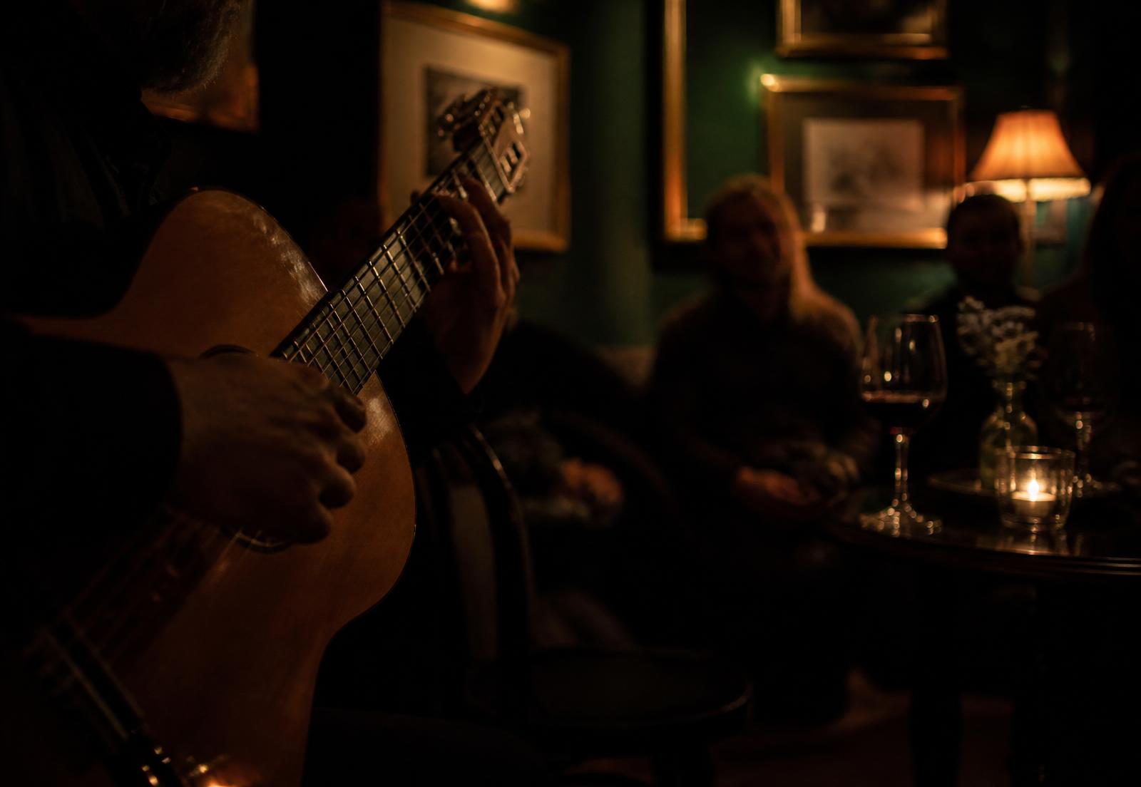 A guitarist silhouetted in warm low light while guests listen